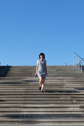 A woman striped dress quickly descends a wide staircase in the city.