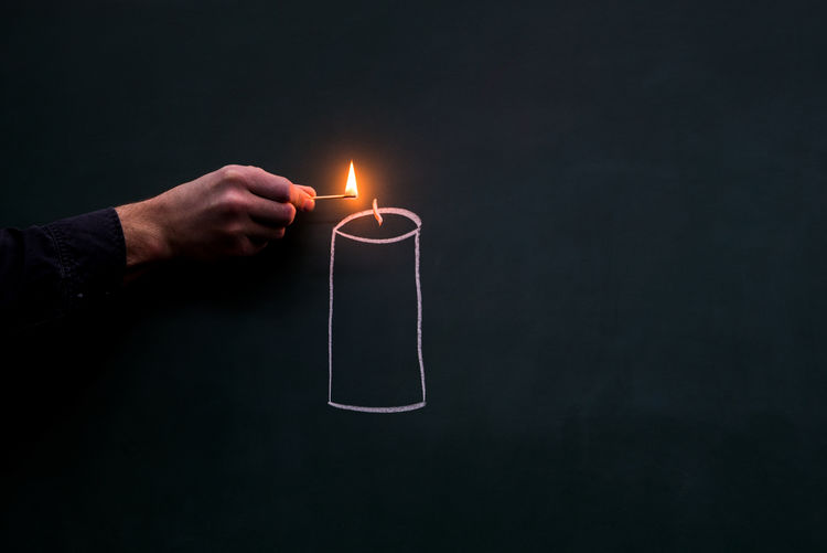 Midsection of man holding illuminated candles against black background