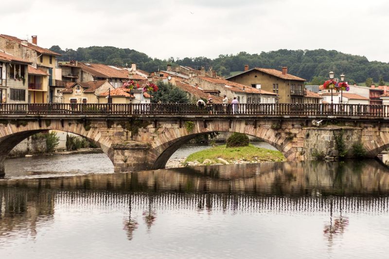 View of bridge over river by houses with trees against cloudy sky