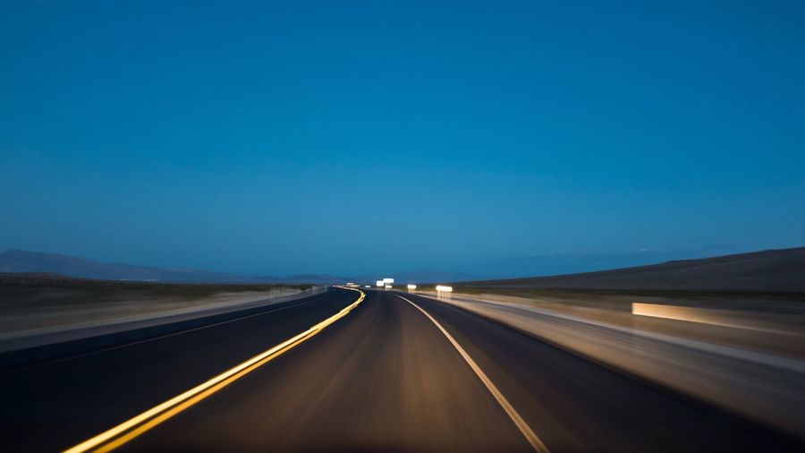Light trails on road against clear blue sky at dusk