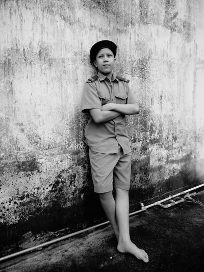 Boy with arms crossed wearing police uniform while standing by weathered wall