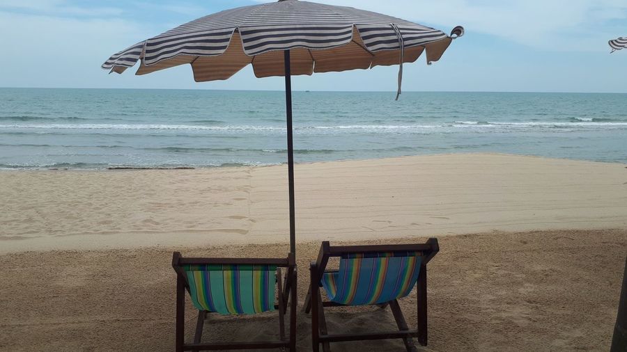 Deck chairs on beach against sky