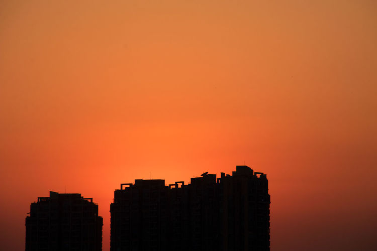 Silhouette buildings against orange sky