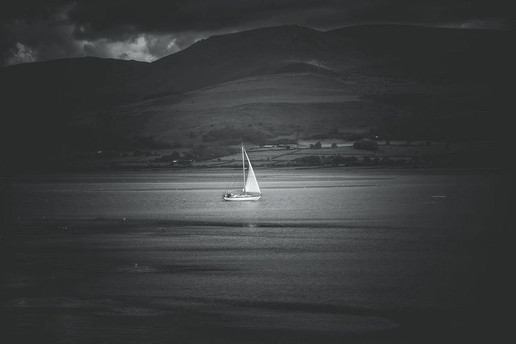 Sailboat in sea against mountains