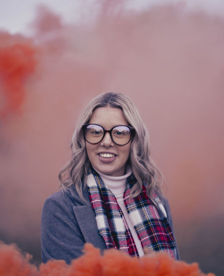 Portrait of young woman standing against orange smoke
