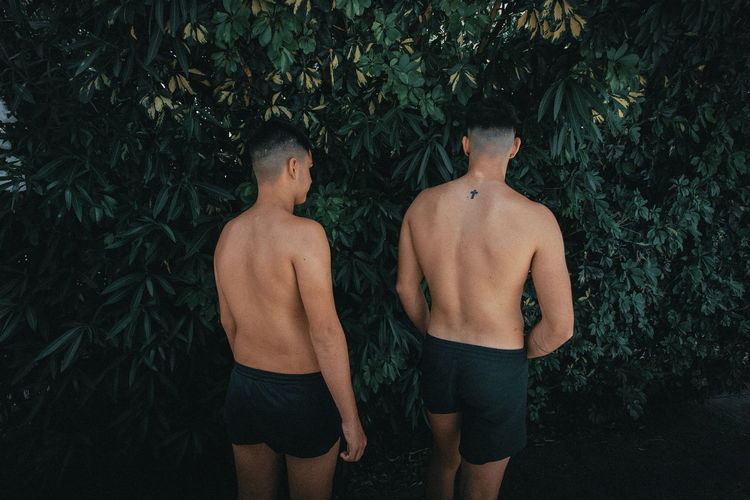 Rear view of shirtless men standing against trees