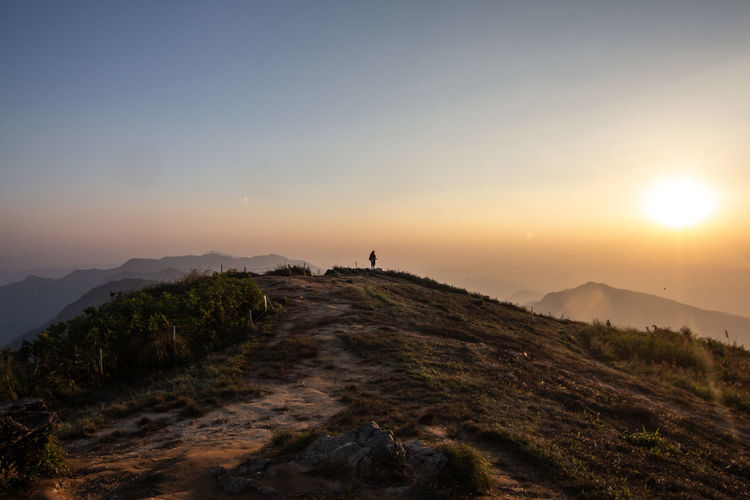 Mid distance view of person standing on mountain against sky during sunset
