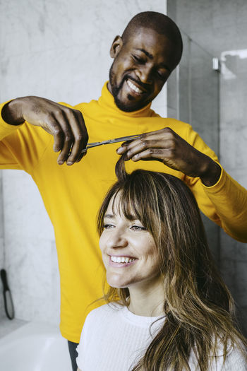 Smiling mid adult man cutting girlfriend hairs at home