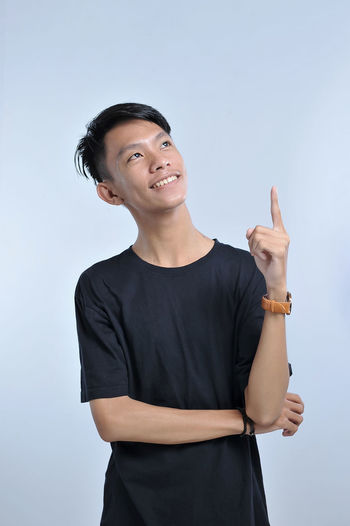 A portrait of a young asian man getting an idea hand gesture. pointing up to copy space. pointing with the index finger a great idea