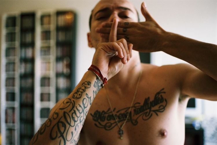 Close-up of shirtless man with tattoo gesturing at home