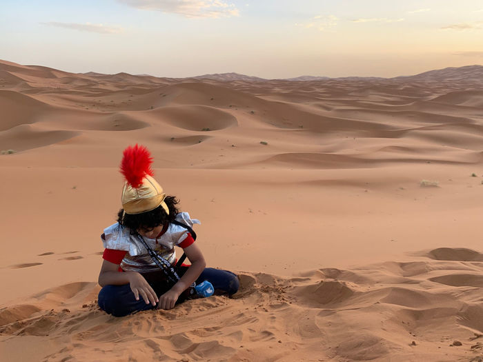 Boy sitting on sand dune in desert