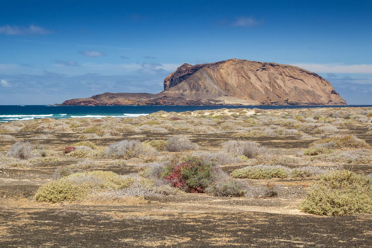Scenic deserted view of large island rock formation and ocean against sky