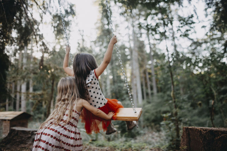 Rear view of girl pushing sister on swing at backyard