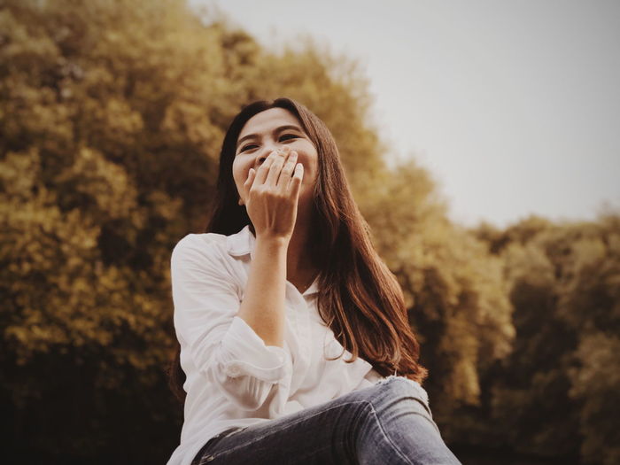 Low angle view of woman with hands covering mouth against trees