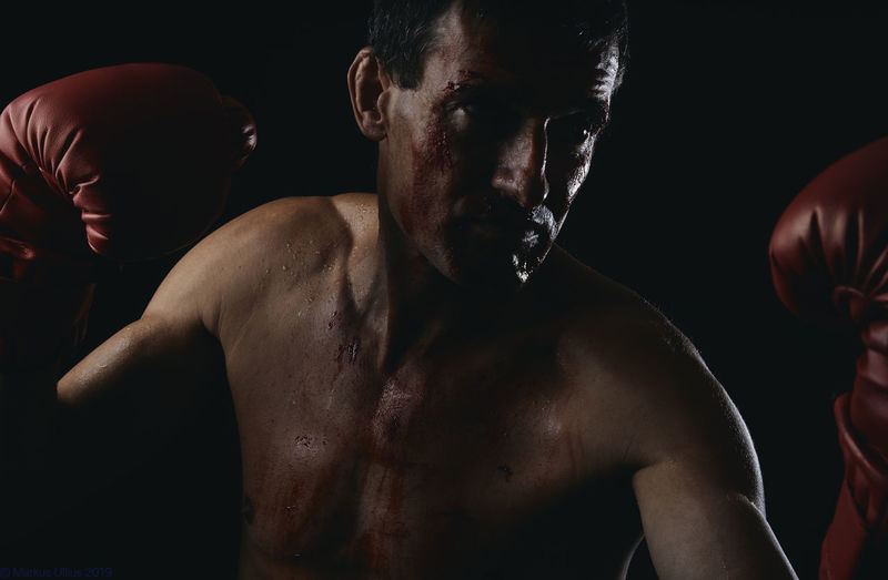  shirtless man with boxing glove standing against black background