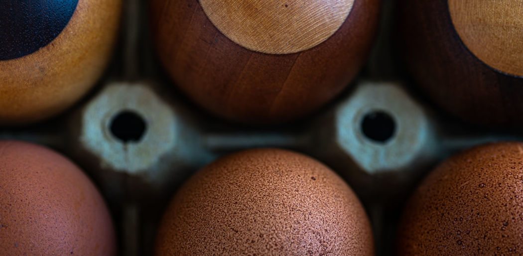 Three fresh eggs close to three wooden eggsmade of pear, oak, wenge and maple wood.