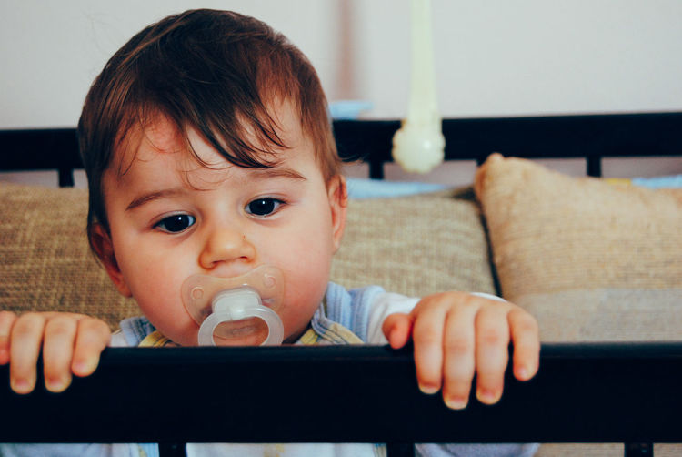 Portrait of cute baby girl sucking pacifier in crib