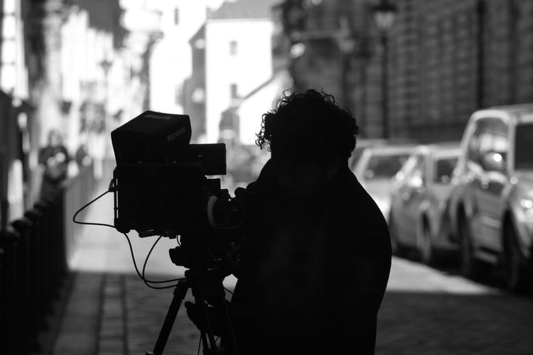 Silhouette man filming with television camera on street