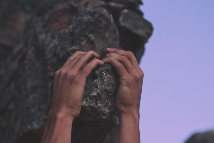 Close-up of hand holding rock against sky