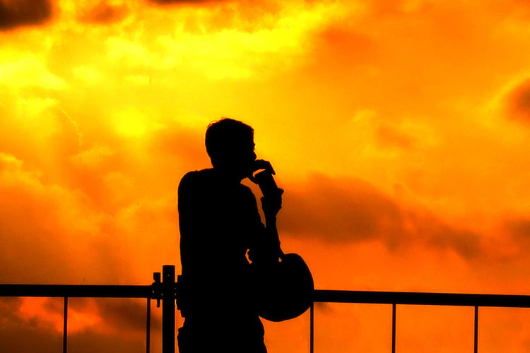 Silhouette of person photographing orange sky