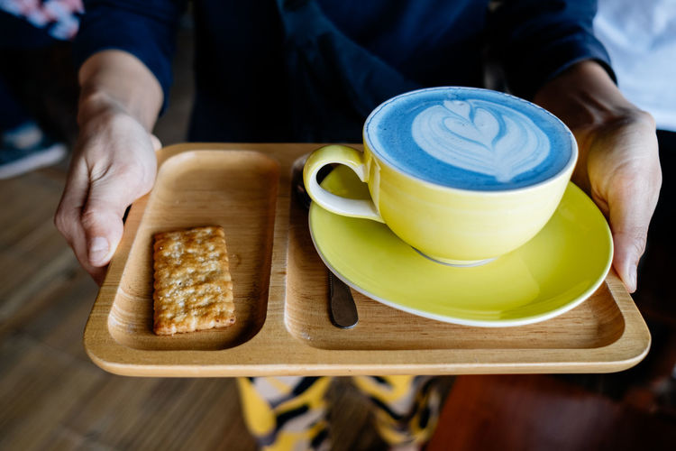 Midsection of person holding coffee cup with cookie in tray