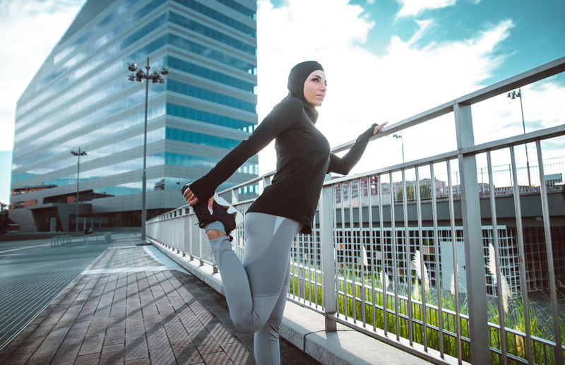 Beautiful woman wearing hijab exercising against building during sunrise