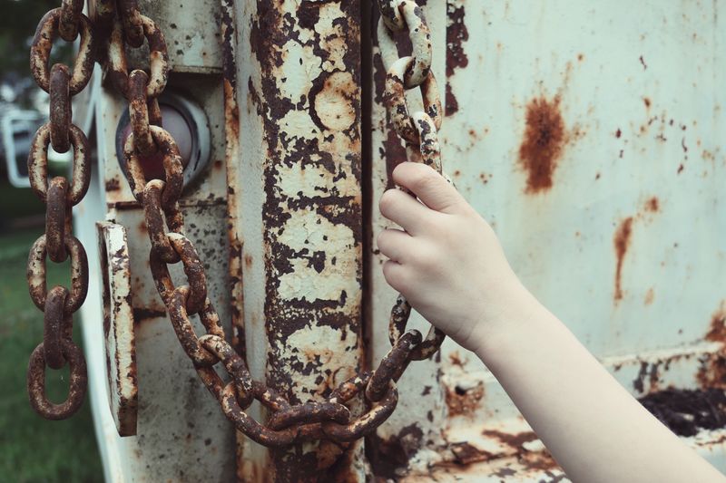 Close-up of human hand holding chain on dumpster