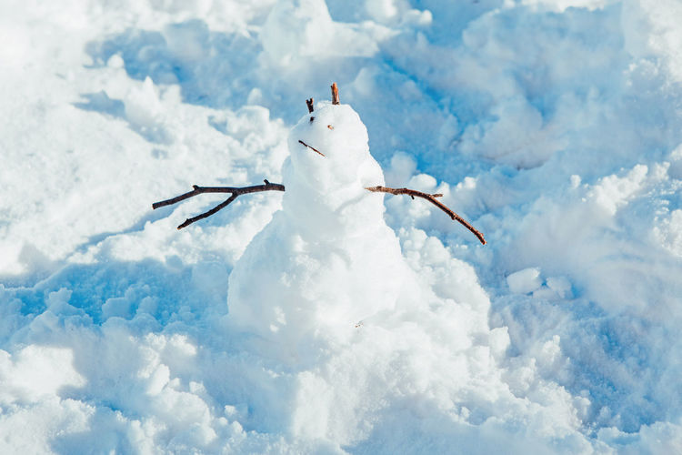 Funny cute small snowman standing in snow during cold winter sunny bright day. 