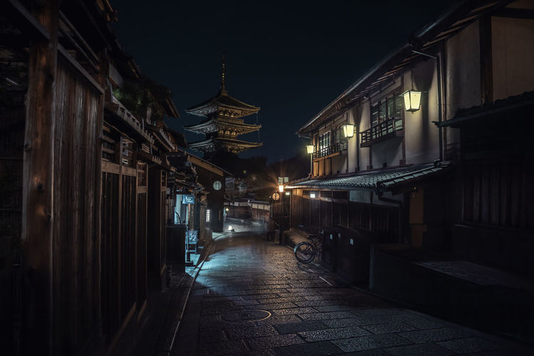 Empty illuminated alley amidst buildings at night