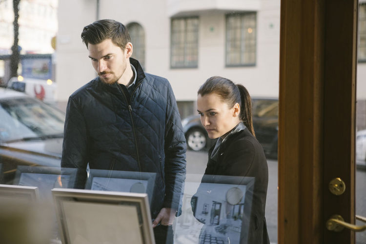 Young couple looking at picture frames on display seen from office window