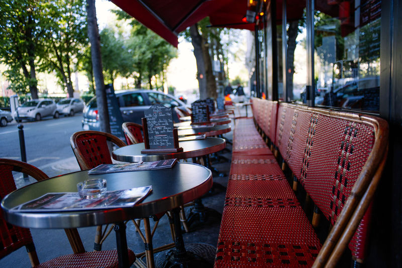 Empty chairs and tables at sidewalk cafe in city