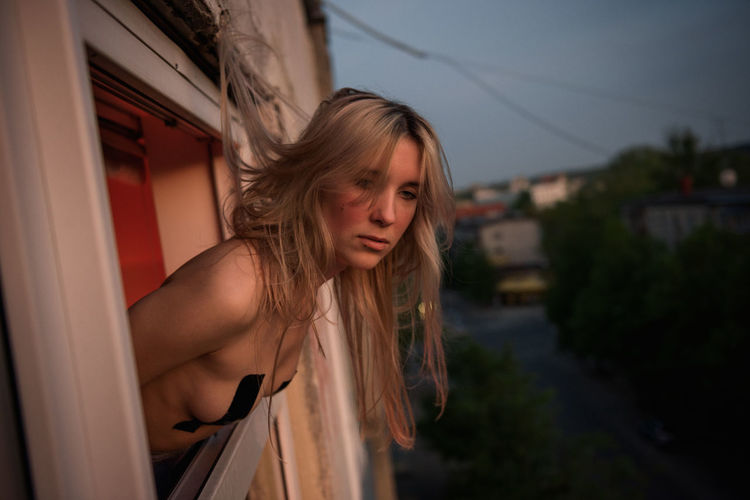 Young topless woman looking through window in city at night