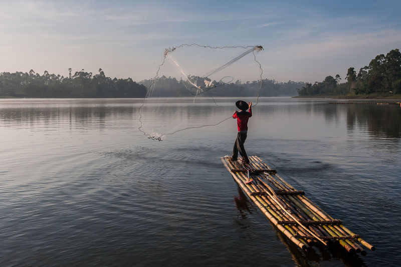Fisherman fishing in lake against sky