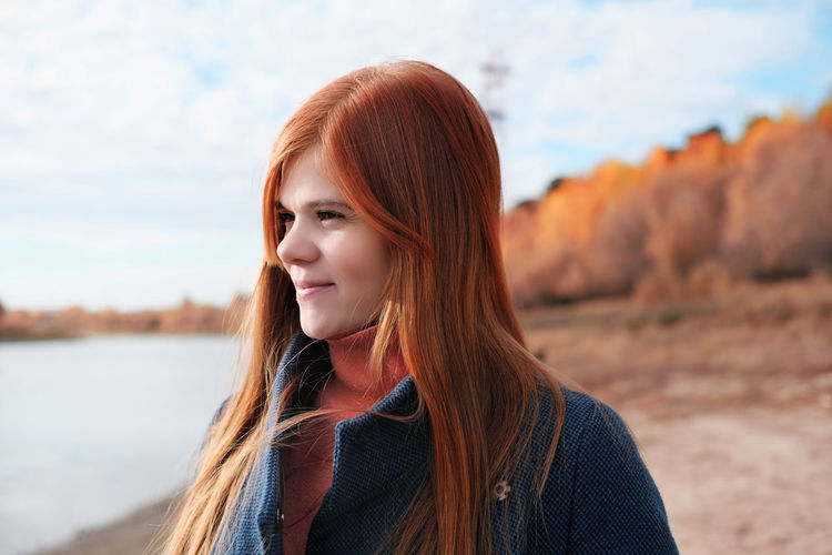 Portrait of happy young red haired woman smiling and looking aside. local travel. 
