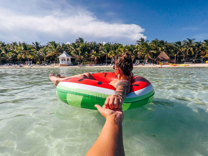 Cropped hand of woman holding female friend floating on inflatable ring in sea