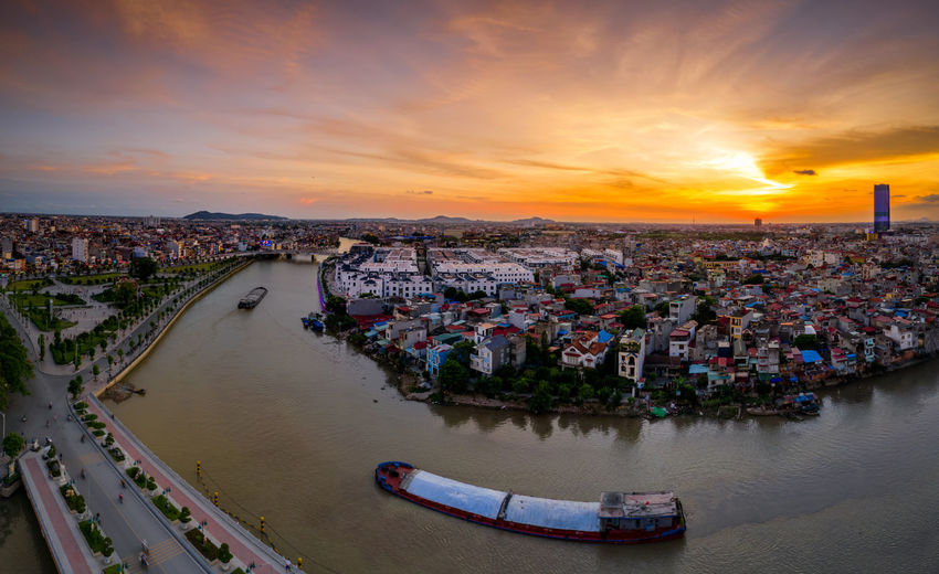 High angle view of buildings by river against sky during sunset