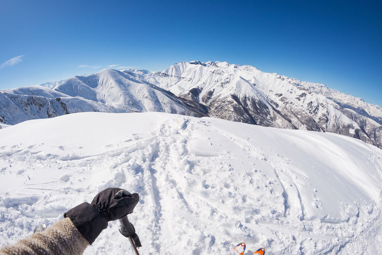Low section of person on snowcapped mountain against clear blue sky