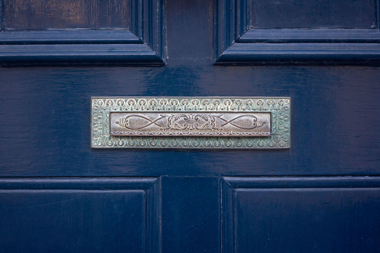 An ornate antique letterbox in a blue wooden front door in london 