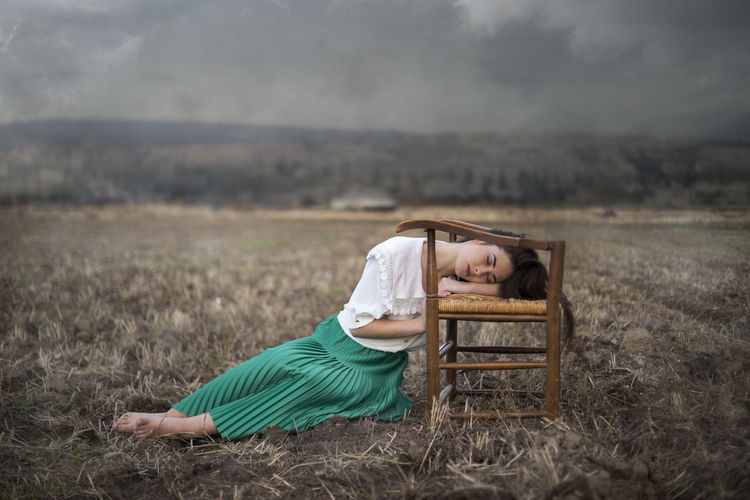 Romantic woman with vintage clothes lying on a chair and the field in the background