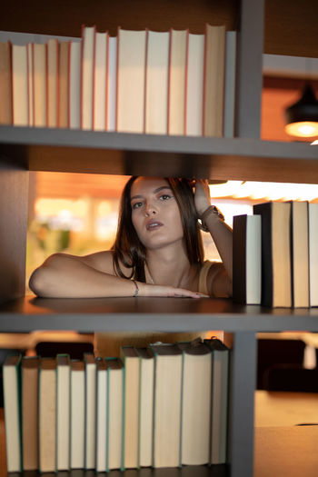 Portrait of young woman leaning on bookshelf at library