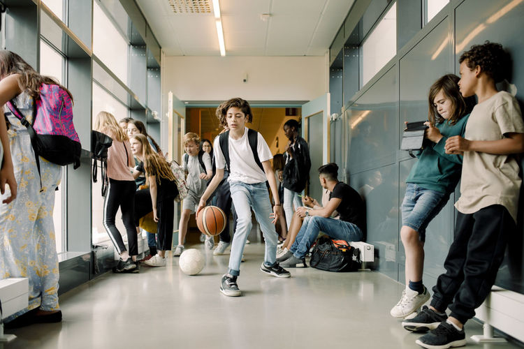Male student playing with basketball during lunch break in school corridor
