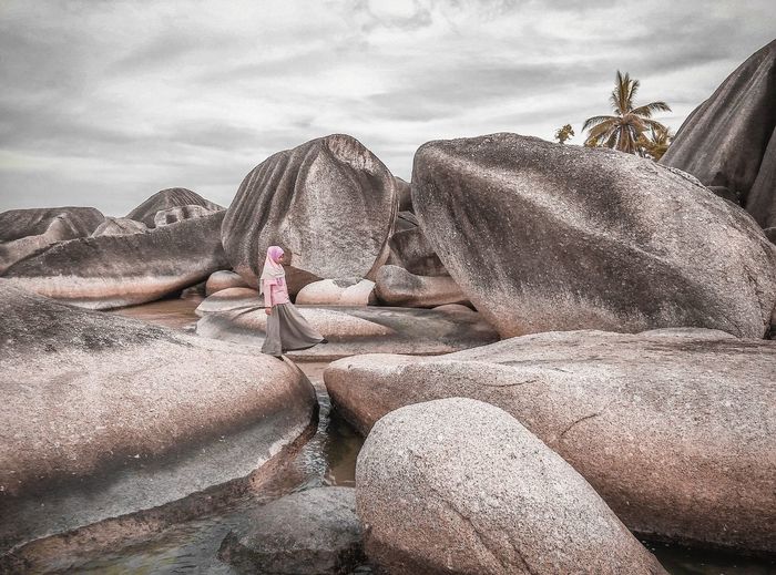 Woman on rocks by sea against sky