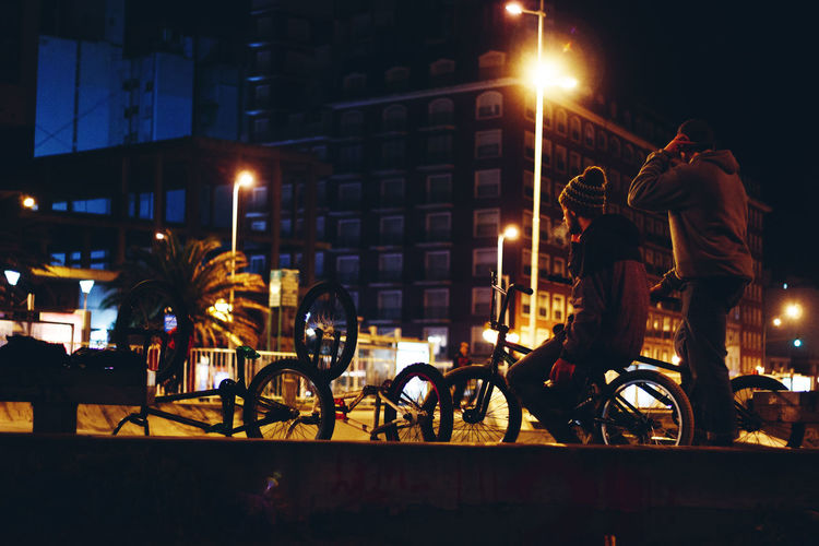 People riding bicycles on illuminated street at night