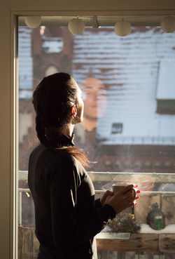SIDE VIEW OF MAN LOOKING THROUGH WINDOW AT HOME