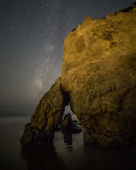 Rock formation by sea against sky at night