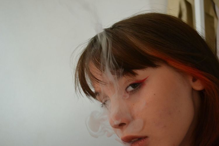 Close-up portrait of woman smoking against white background