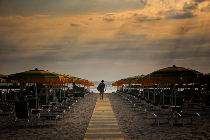 Rear view of man standing on chairs against sky during sunset