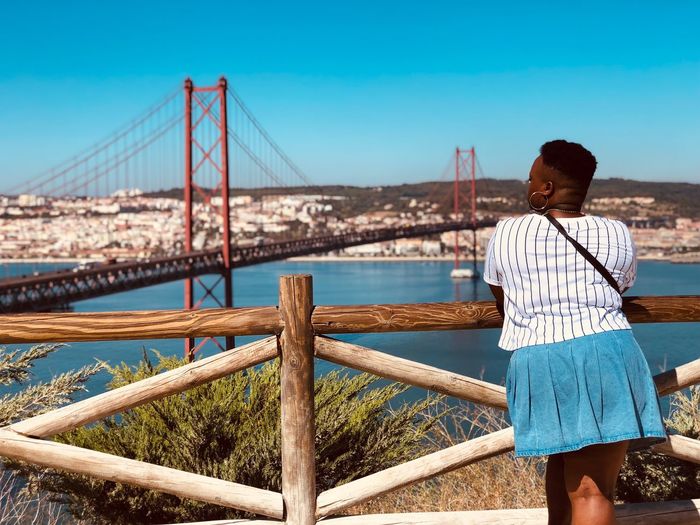 Rear view of woman looking at april 25th bridge over tagus river against sky