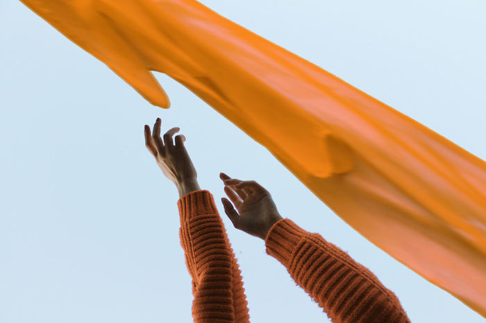 Cropped hands by orange textile against clear sky