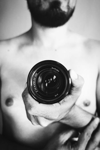 Midsection of shirtless man holding camera lens